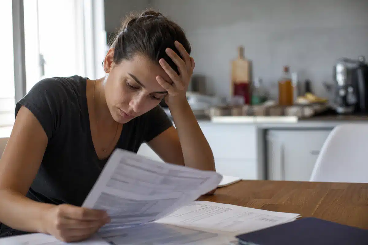Femme à table, préoccupée, triant des factures